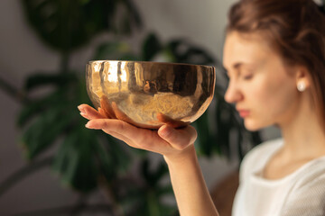 Young woman playing on a singing tibetian bowl.Relaxation and meditation.Sound therapy,alternative medicine.Buddhist healing practices.Clearing the space of negative energy.Selective focus,close up. © Tatyana