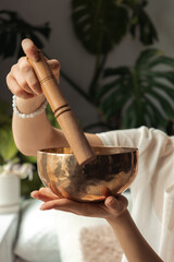 Young woman playing on a singing bowl,hands close up.Relaxation and meditation.Sound therapy,alternative medicine.Buddhist healing practices.Clearing the space of negative energy.Selective focus.