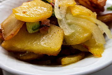 Close-up of delicious, golden yellow fried fried potatoes with bacon and onions