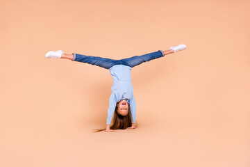 Full body photo of sportive funny pupil standing arms upside down split legs isolated on beige...