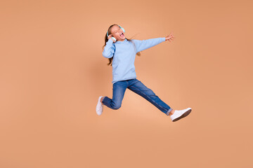 Fototapeta na wymiar Full body portrait of overjoyed carefree person jump arm touch headphones isolated on beige color background