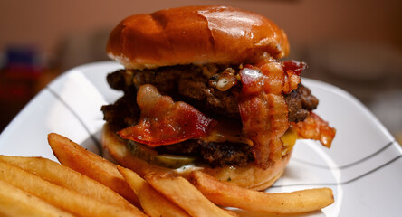 Triple decker hamburger with bacon strips and a side of french fries.