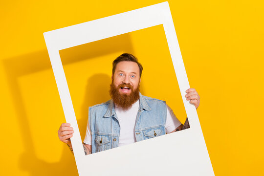 Photo of impressed funky guy dressed denim vest holding looking white photo frame isolated yellow color background
