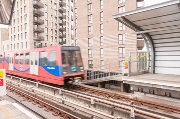 Fototapeta na wymiar Blurred motion, DLR Docklands Light Railway train at Pontoon Dock Station in London. DLR train arriving the station on a bright day, Canning Town, London, England, June 19, 2022 