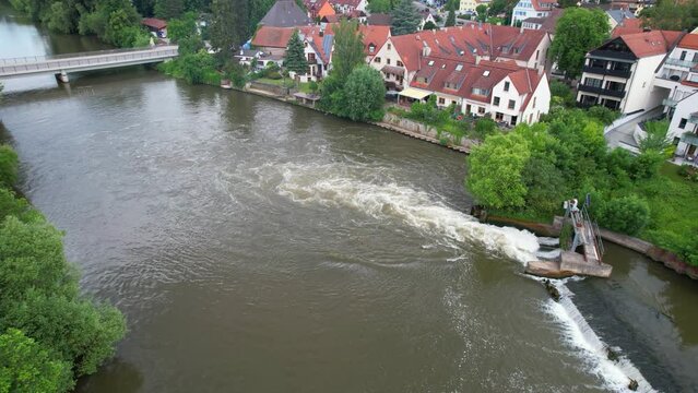 Slow Motion drone footage of water running through a barrier  at the river Regnitz and the suburb of Erlangen-Bruck
