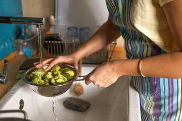 Woman washes broccoli in the sink