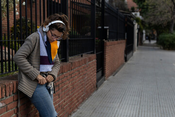 A young Latin American girl listens to music with her headphones while standing on a city sidewalk