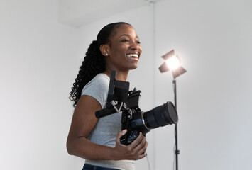 African American Female Videographer Posing with Video Camera in Hand on Film Set. Camera Woman is...