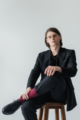 Elegant brunette man sitting on chair isolated on grey.