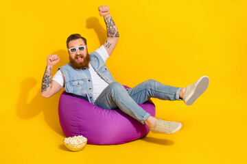 Photo of funny lucky guy dressed denim vest sitting bean bag eating pop corn watching movie empty...