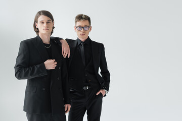 Young gay couple in formal wear posing isolated on grey.