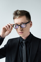 Portrait of young man i formal wear holding eyeglasses looking at camera isolated on grey.