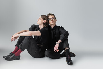 Young and stylish homosexual couple sitting on grey background.