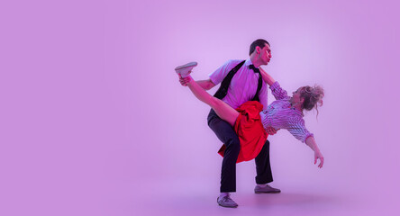 Stylish young man and pretty woman in vintage style outfits dancing retro dance isolated on very peri color background in neon light.