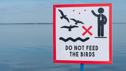 Sign over water to not feed the birds. Do not feed the birds warning sign on water background.