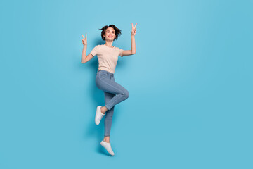 Fototapeta na wymiar Full length photo of shiny cute lady dressed beige t-shirt jumping high showing v-signs empty space isolated blue color background
