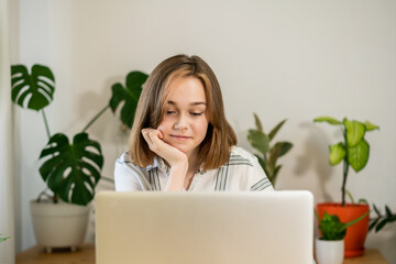 Beautiful young woman entrepreneur working on laptop at home. Female freelancer working at home office. Girl using a computer for study online at home. Remote work or study concept.