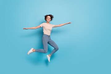 Fototapeta na wymiar Full length photo of funny shiny lady dressed beige t-shirt jumping arms sides empty space isolated blue color background