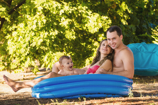 Mom, dad and little boy play in an inflatable pool near a sun lounger on the lawn/ Family in swim wear tanning
