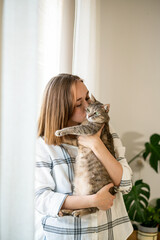 Indoor shot of amazing lady holding pet. Portrait of young woman holding cute striped cat with green eyes. Female hugging her cute kitty. Adorable domestic pet concept. Indoor shot of amazing lady