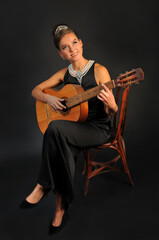 Fototapeta premium Girl with a guitar in a black dress on a black background
