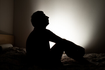 Male silhouette depicting loneliness or depression sitting in his apartment bed