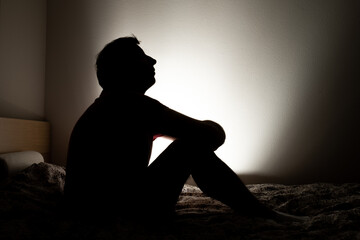 Male silhouette depicting loneliness or depression sitting in his apartment bed