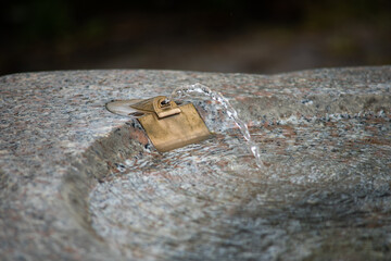 Public drinking water fountain, clear water flowing from metal faucet. Telephoto shot, shallow depth of field, no people