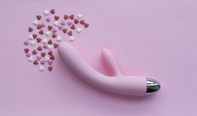 Pink vibrator toy for adults lies on a pink background, next to decorative hearts mimic an orgasm. Conceptual photo. - 512785984