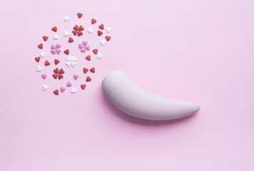 Pink vacuum stimulator toy for adults lies on a pink background, next to the decorative hearts mimic an orgasm. Conceptual photo. - 512785985