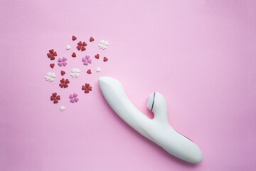 White vibrator toy for adults lies on a pink background, next to decorative hearts mimic an orgasm. Conceptual photo. - 512785995
