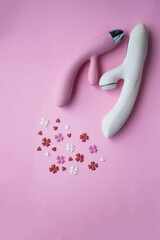 Two vibrators pink and white toy for adults lies on a pink background, next to decorative hearts mimic an orgasm. Conceptual photo. - 512785996