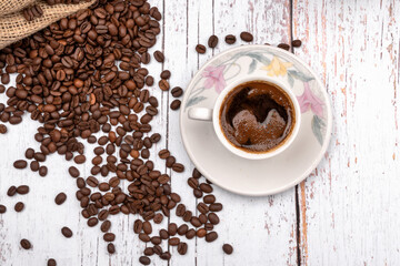 Coffee cup with freshly brewed traditional black coffee and coffee beans on white table. Top view.