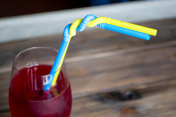 In a glass of wine, two cocktail straws are woven. Yellow and blue tubes are woven like the flag of...