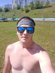sporty man with naked torso, sunglasses and headphones at the city stadium. Selfie portrait on smartphone.