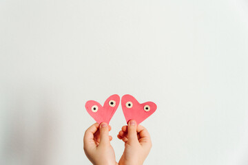 Hand made for Valentines or Mothers day. Two hand painted pink paper hearts with eyes in the child's hands. White background. Copy space