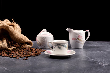 Coffee cup with freshly brewed traditional black coffee, coffee set and coffee beans on black background.
