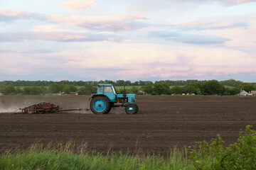 Obraz premium Tractor plowing agricultural field under cloudy sky