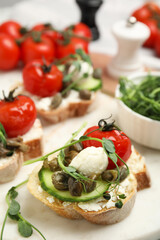 Tasty bruschettas with capers, vegetables and mozzarella served on white marble board, closeup