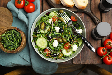 Fresh salad with vegetables, capers and mozzarella in bowl on wooden table, flat lay