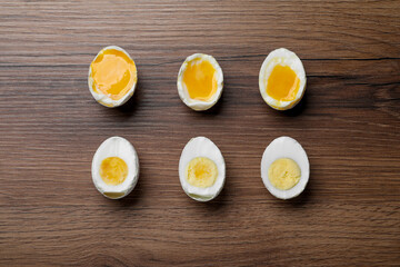 Different readiness stages of boiled chicken eggs on wooden table, flat lay