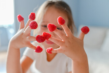 The little girl played with raspberries on her fingers