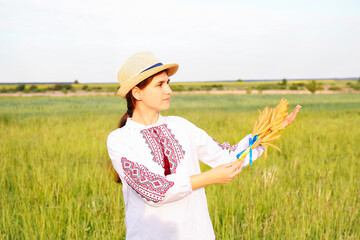 Defocus young woman in vyshyvanka and hat holding bouquet of ripe golden spikelets of wheat and flag on the meadow nature background. Flag Ukraine. Freedom. Honor. Independence day. Out of focus