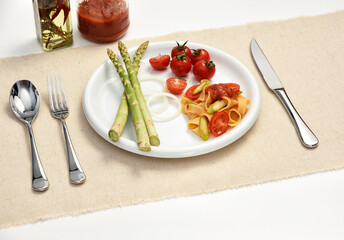 Nutrition food with cherry tomatoes, onion, asparagus and fettuccine in white plate on beige linen table runner, high key