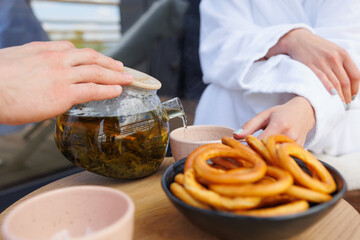 Man pours tea from a teapot into a cup for his woman. couple in bathrobes drinking green tea