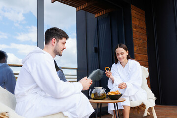 Fototapeta na wymiar Couple in bathrobes drinking tea with bagels after spa treatments