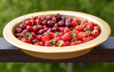 Cherries and strawberries in a copper bowl against the backdrop of nature