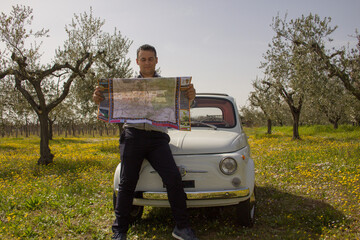 Man consulting a road map leaning against a vintage car after getting lost during a vacation in Italy