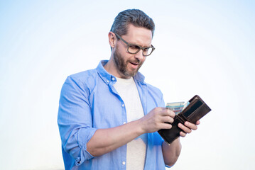 Serious guy in glasses taking cash money out of wallet sky background
