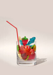 Jelly sugar candies in glass with drinking straw, vertical photo with copy space